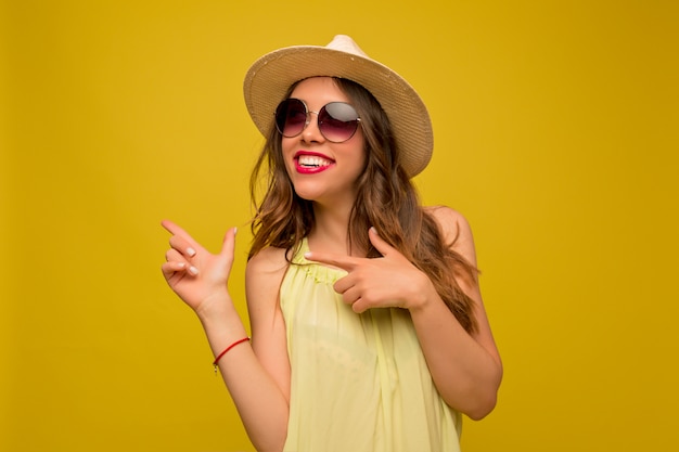 Mujer joven en vestido amarillo con sombrero y gafas de sol