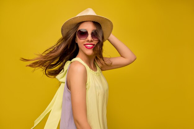 Mujer joven en vestido amarillo con sombrero y gafas de sol