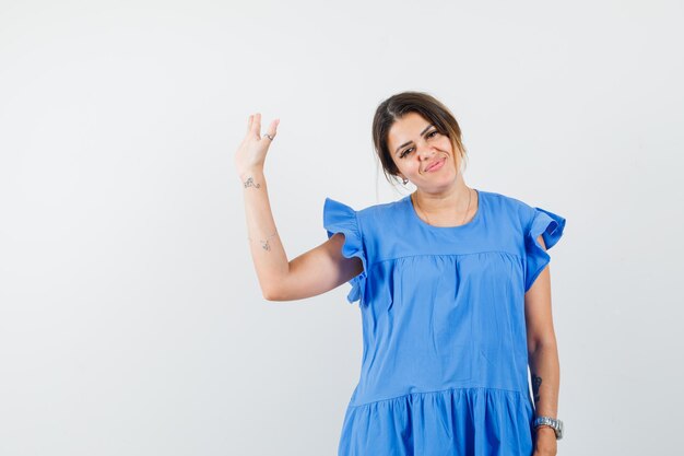 Mujer joven en vestido azul agitando la mano para decir adiós y mirando alegre