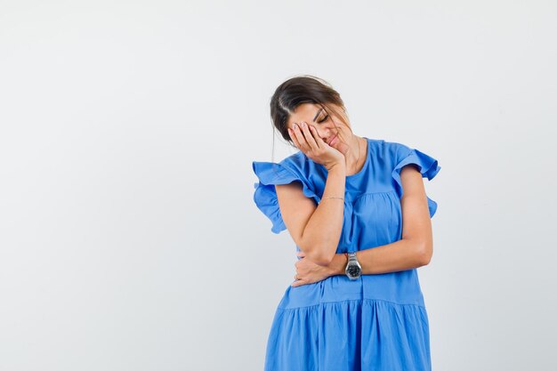 Mujer joven en vestido azul con la cara inclinada en la palma y mirando soñoliento