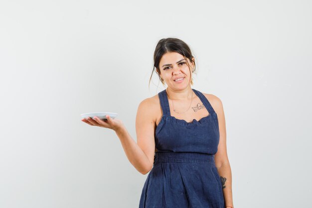 Mujer joven en vestido azul oscuro sosteniendo un platillo vacío y mirando alegre