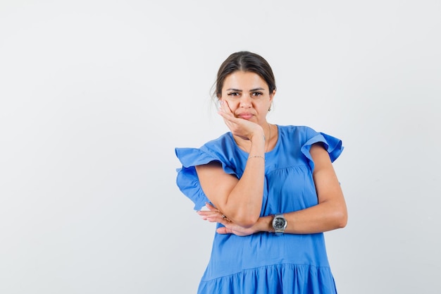 Mujer joven en vestido azul de pie en pose de pensamiento y mirando sensible