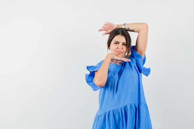 Mujer joven en vestido azul posando con la mano debajo de la barbilla y mirando bastante