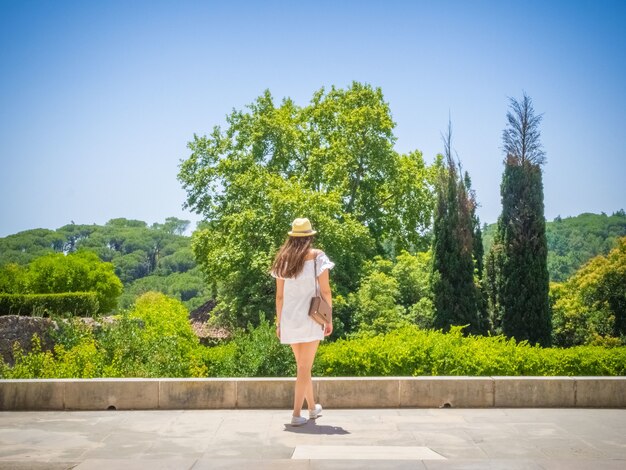 Mujer joven con un vestido blanco caminando en un parque disfrutando de la hermosa vista de un bosque verde