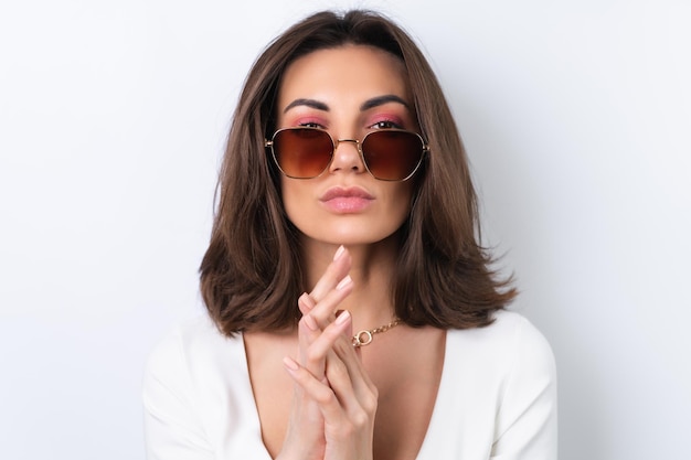 Mujer joven en un vestido de cóctel cadena de oro brillante maquillaje rosa primaveral sobre un fondo blanco En elegantes gafas de sol de moda