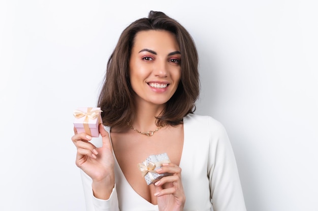 Mujer joven en un vestido de cóctel cadena de oro maquillaje rosa primavera brillante sobre un fondo blanco sostiene una caja de regalo para el 8 de marzo y sonríe alegremente