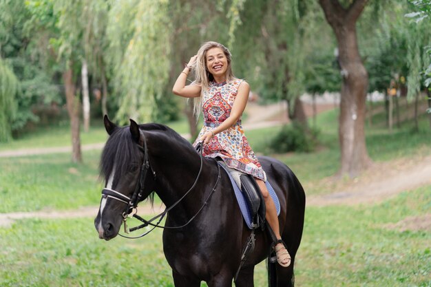 Mujer joven en un vestido colorido brillante montando un caballo negro