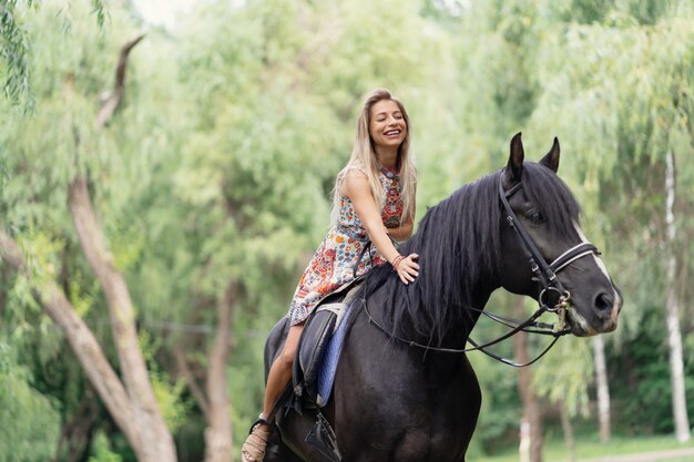 Mujer joven en un vestido colorido brillante montando un caballo negro