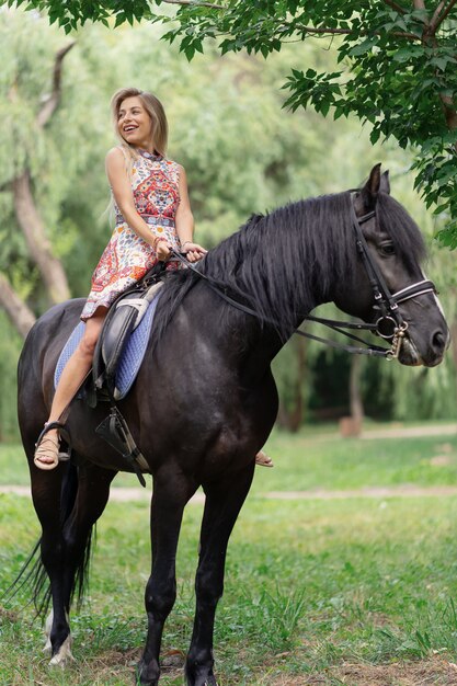 Mujer joven en un vestido colorido brillante montando un caballo negro