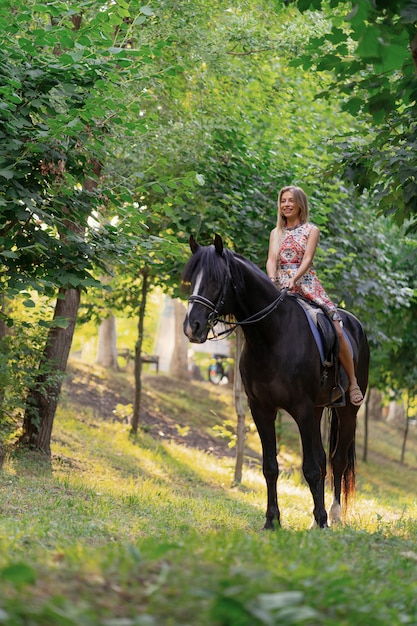 Mujer joven en un vestido colorido brillante montando un caballo negro