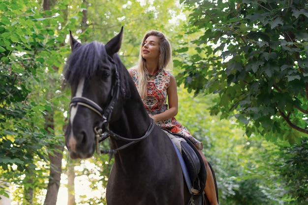 Mujer joven en un vestido colorido brillante montando un caballo negro