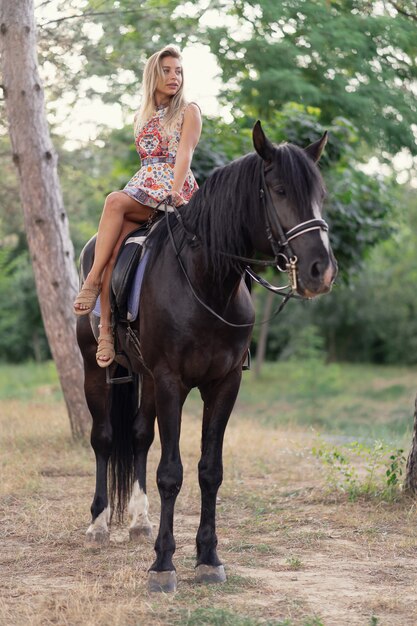 Mujer joven en un vestido colorido brillante montando un caballo negro