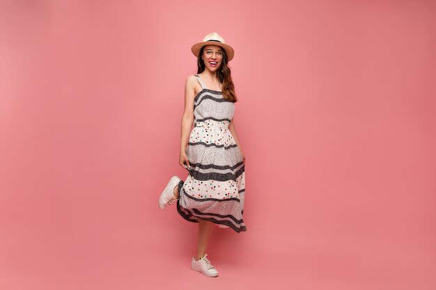 Mujer joven en vestido gris con sombrero y gafas