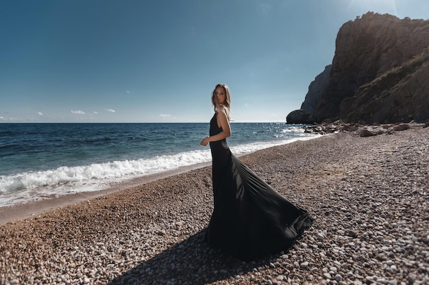 Foto gratuita mujer joven en vestido negro de moda en la playa