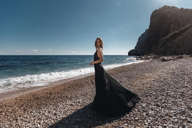 mujer joven en vestido negro de moda en la playa