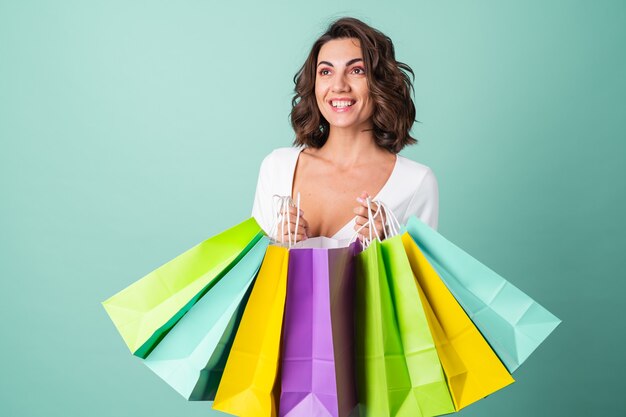 Mujer joven en un vestido de noche blanco sobre verde claro con maquillaje rosa brillante tiene bolsas de compras