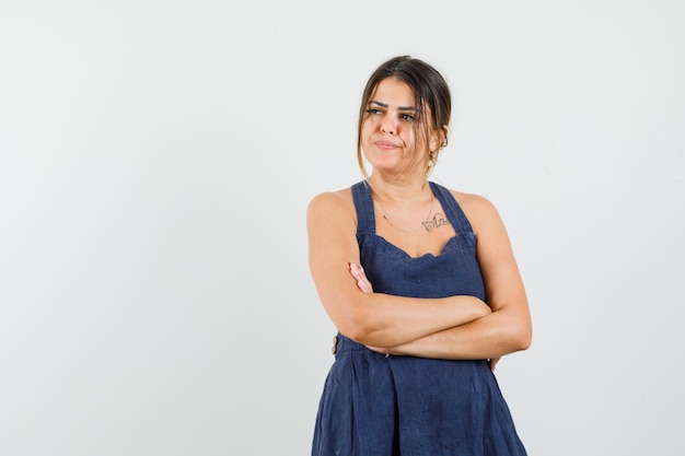 Mujer joven en vestido de pie con los brazos cruzados y mirando pensativo