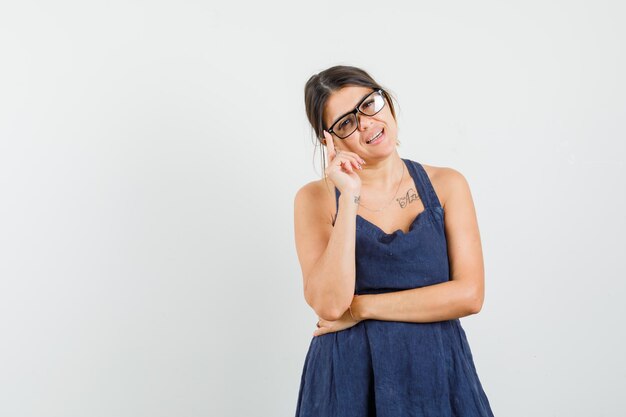 Foto gratuita mujer joven en vestido de pie en pose de pensamiento y mirando inteligente