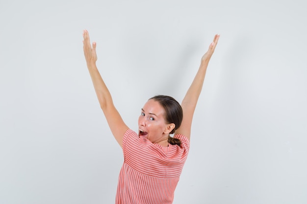 Foto gratuita mujer joven en vestido de rayas levantando los brazos mientras mira hacia atrás y parece feliz, vista posterior.