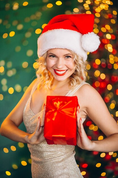 Mujer joven en vestido con regalos de Navidad por el árbol de Navidad