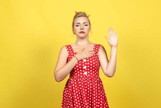 Mujer joven en vestido rojo de lunares levantando emocionalmente una mano en amarillo