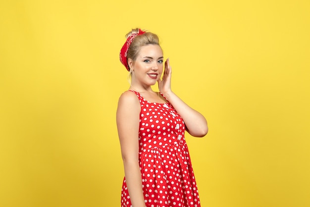 Foto gratuita mujer joven en vestido rojo de lunares de pie y posando en amarillo