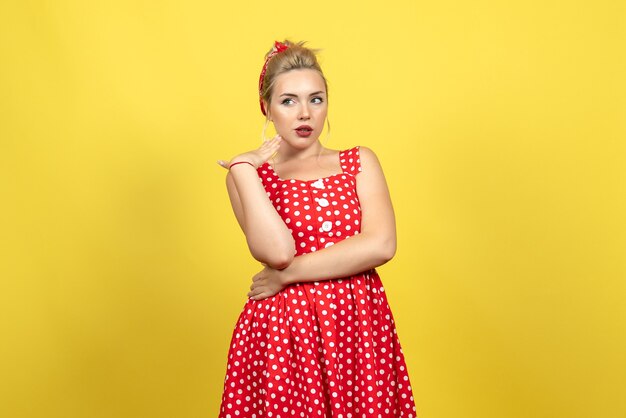 mujer joven en vestido rojo de lunares de pie y posando en amarillo