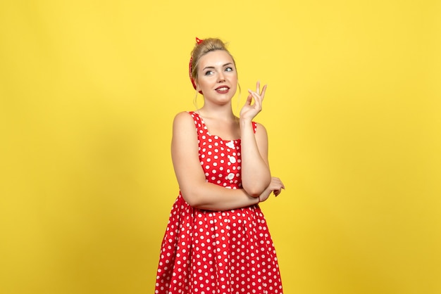 Mujer joven en vestido rojo de lunares de pie y posando en el piso amarillo mujer mujer color lindo vestido de moda