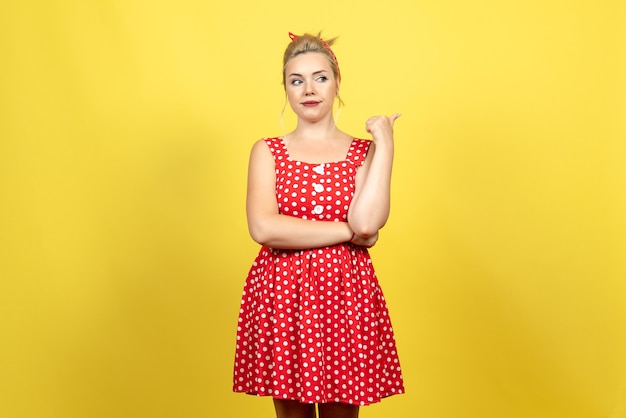 mujer joven en vestido rojo de lunares posando en amarillo claro
