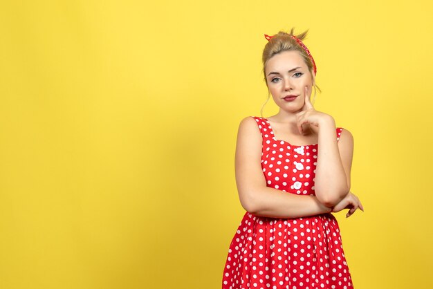 mujer joven en vestido rojo de lunares posando en amarillo