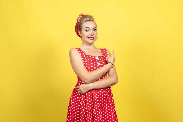 mujer joven en vestido rojo de lunares posando en amarillo