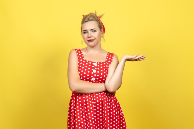 mujer joven en vestido rojo de lunares posando en amarillo