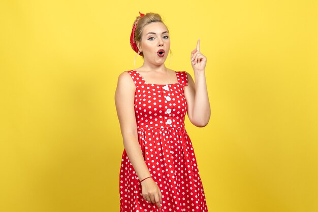 mujer joven en vestido rojo de lunares posando en amarillo