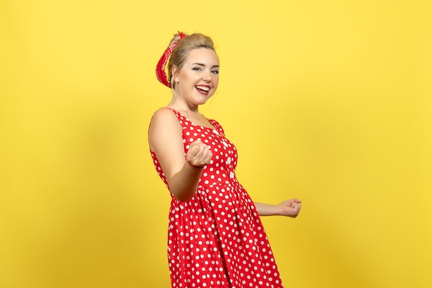 Mujer joven en vestido rojo de lunares posando emocionalmente en amarillo claro