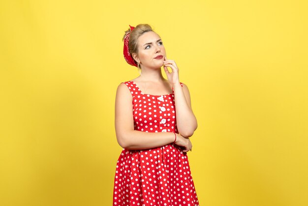 Mujer joven en vestido rojo de lunares posando y pensando en amarillo