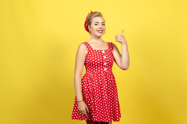 mujer joven en vestido rojo de lunares posando y sonriendo en amarillo