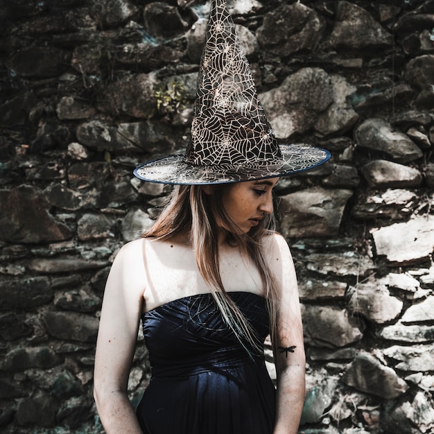 Foto gratuita mujer joven en vestido y sombrero de bruja mirando a un lado