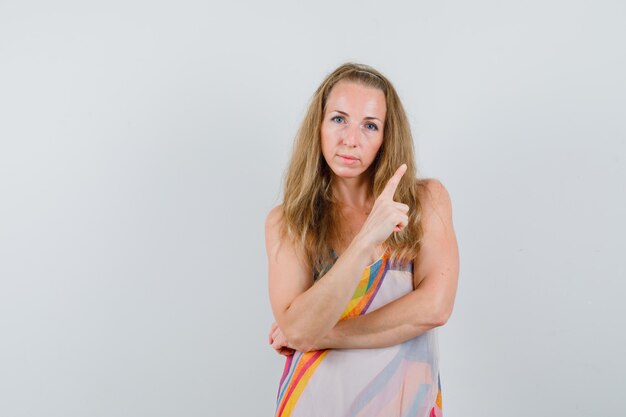 Foto gratuita mujer joven en vestido de verano apuntando hacia arriba y mirando sensible