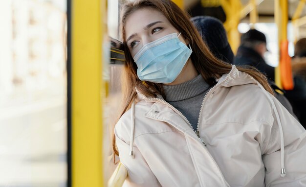 Mujer joven viajando en autobús urbano con mascarilla quirúrgica