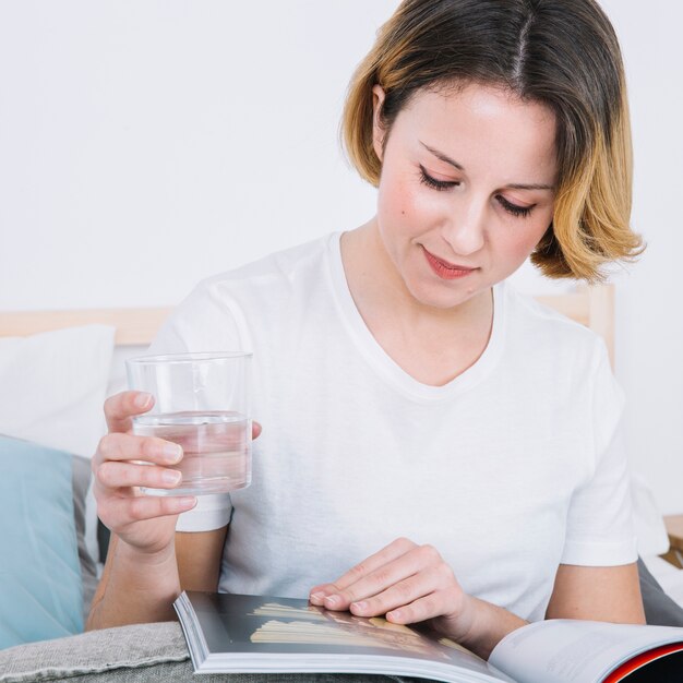 Mujer joven con vidrio disfrutando revista