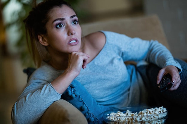 Mujer joven viendo una película con anticipación mientras come palomitas de maíz por la noche en casa