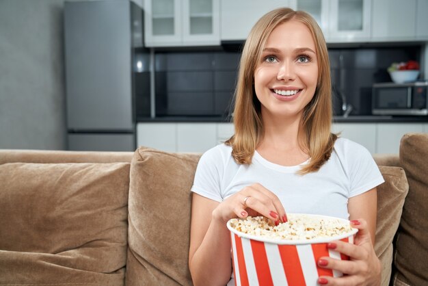 Mujer joven viendo una película y comiendo palomitas de maíz en casa