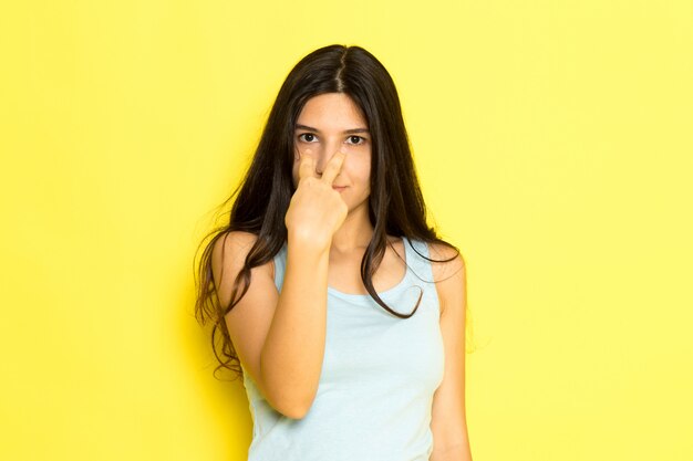 Una mujer joven de vista frontal en camisa azul posando apuntando a sus ojos sobre el fondo amarillo pose de niña modelo belleza joven