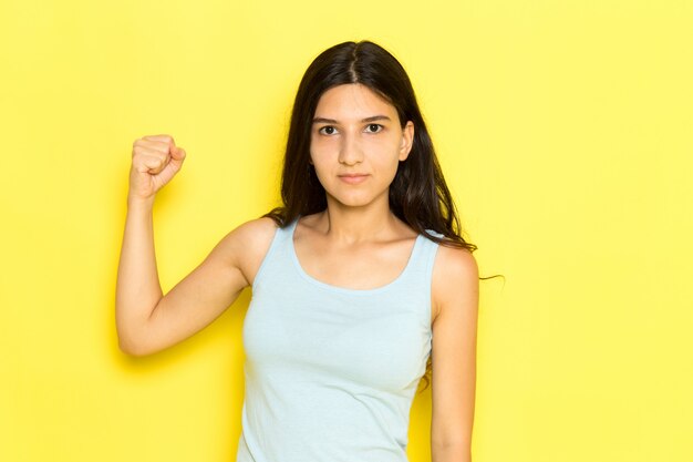 Una mujer joven de vista frontal en camisa azul posando con expresión enojada y nudillo en el fondo amarillo pose de niña modelo belleza joven