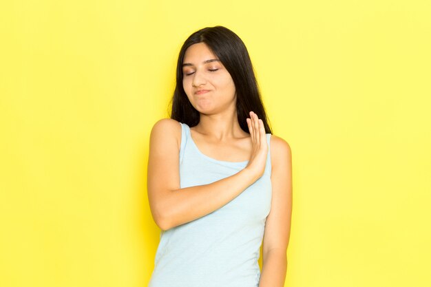 Una mujer joven de vista frontal en camisa azul posando en el modelo de pose de niña de fondo amarillo