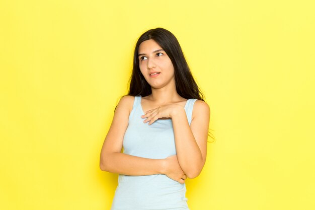 Una mujer joven de vista frontal en camisa azul posando en el modelo de pose de niña de fondo amarillo