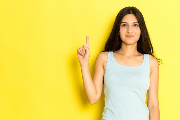 Una mujer joven de vista frontal en camisa azul posando y msiling sobre el fondo amarillo pose de niña modelo belleza joven