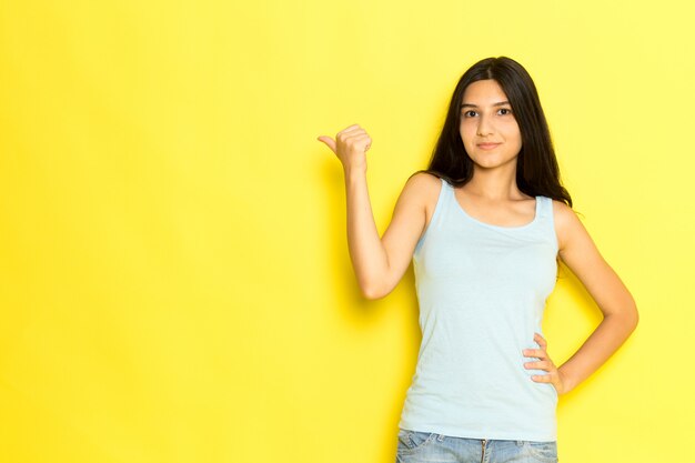 Una mujer joven de vista frontal en camisa azul posando y señalando con sus dedos sobre el fondo amarillo pose de niña modelo belleza joven