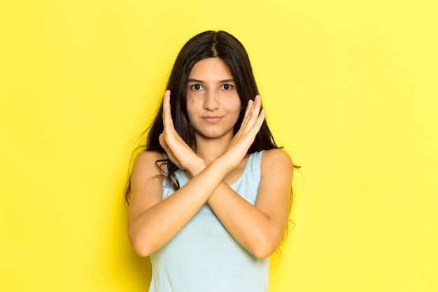 Una mujer joven de vista frontal en camisa azul posando showign signo de prohibición sobre el fondo amarillo pose de niña modelo belleza joven