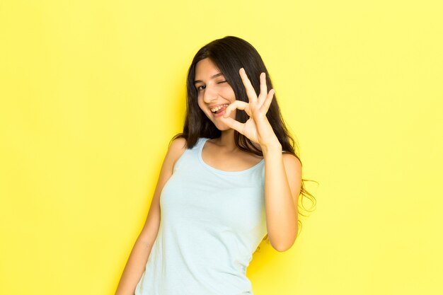 Una mujer joven de vista frontal en camisa azul posando sonriendo y mostrando bien el signo